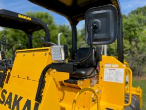 Optional mirror kit installed on a SAKAI SV204 roller compactor which also shows the optional LED work lights.